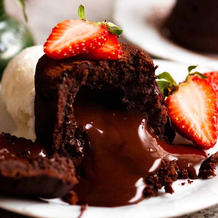 Close up of Molten Chocolate Cake with chocolate lava pouring out, decorated with strawberries and a scoop of ice cream