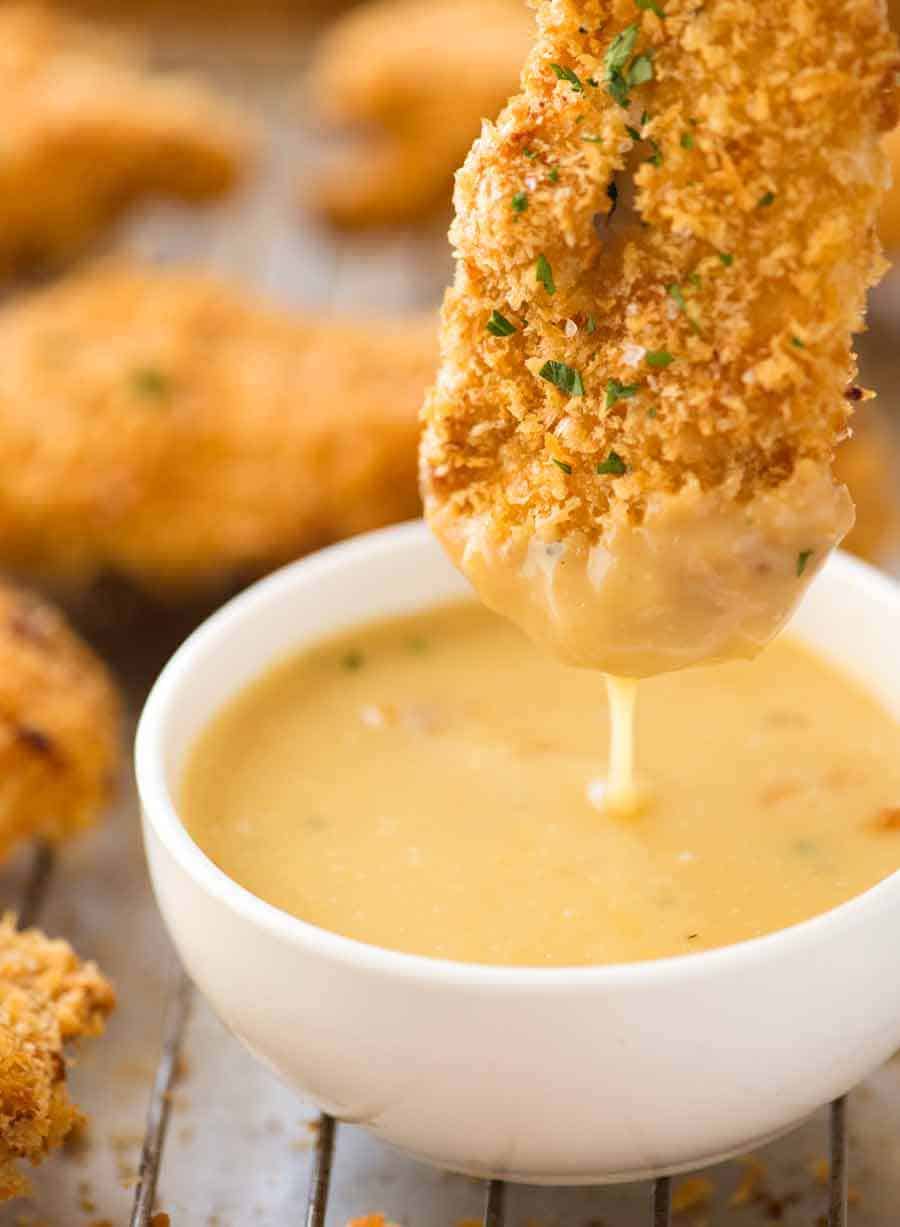 Crunchy Baked Chicken Tenders being dipped into Honey Mustard sauce