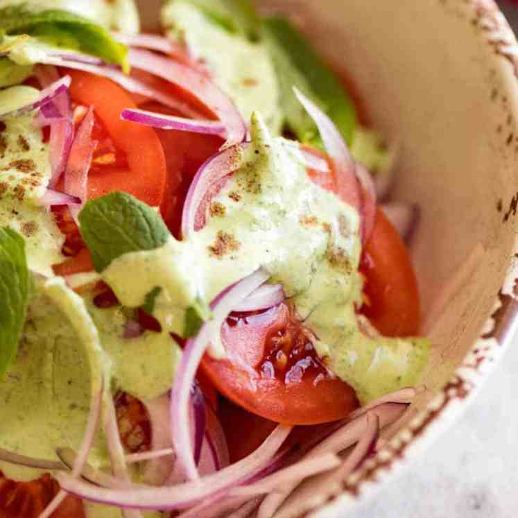 Close up of Indian Tomato Salad drizzled with Mint Dressing in a rustic cream bowl, ready to be served