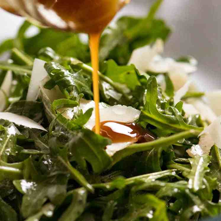 Close up of Balsamic Dressing being drizzled over rocket salad with shaved parmesan