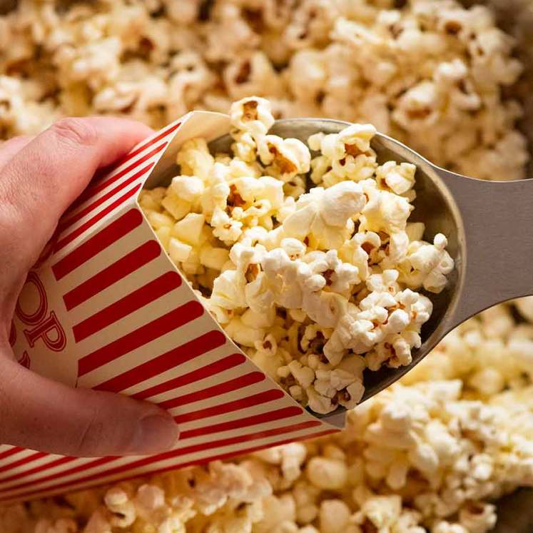 Scooping Slightly sweet and salty butter popcorn into popcorn holder