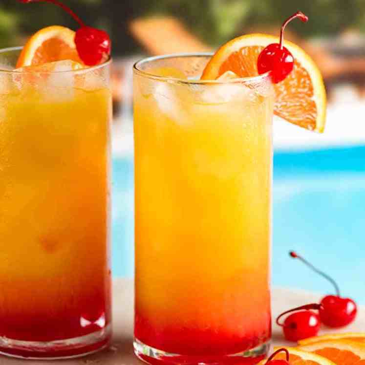 Two Tequila Sunrise cocktails by a pool, garnished with orange slice and maraschino cherries ready to drink